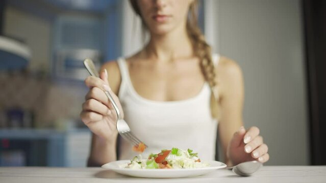 A woman is eating fresh vegetable salad while sitting in her kitchen. Slim woman is observing diet and counting calories. Concept of healthy lifestyle or proper nutrition and weight loss.