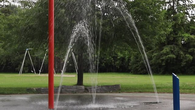 Splash pad and swings at playground in local public park on summer day. Fountain with running water
