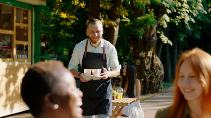 In the middle of park at coffee terrace group of multiethnic ladies enjoy the time together barista brings fresh coffee ladies takes the coffee and start to conversation they are smiling and feeling