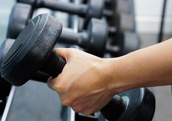 Fototapeta na wymiar Close up of hand holding dumbbell in fitness. Concept of exercise, healthy and lose weight.