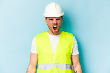 Young laborer caucasian man isolated on blue background screaming very angry and aggressive.