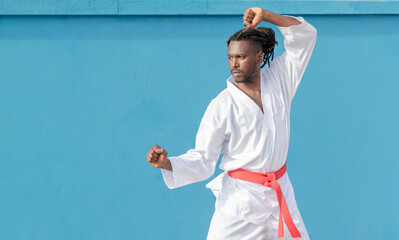 a young african american man training taekwondo outdoors on a blue background