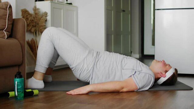 A plump guy in sportswear, lying on a mat, performs exercises. Sport