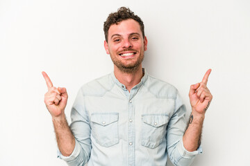 Young caucasian man isolated on white background indicates with both fore fingers up showing a...
