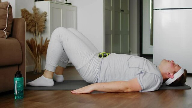 A plump guy in sportswear, lying on a mat, performs exercises. Sport