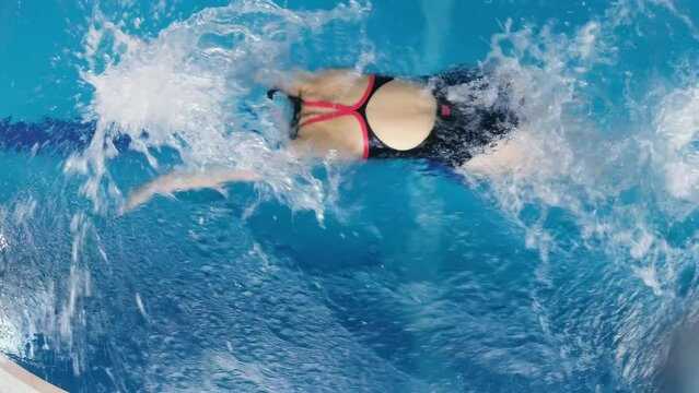 sportswoman swimmer in a tracksuit, in diving goggles, in a swimming cap is training in the pool. The athlete swims in butterfly style. Wide angle, 4k