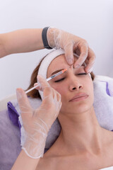 Close up of beautician expert's hands injecting botox in female forehead