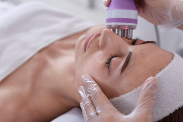 A young woman undergoing a facial radiofrequency face lift treatment. Facial skin care treatment, anti-aging facial rejuvenation. Beauty and dermatology concept.