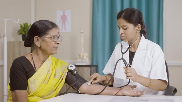 Woman Doctor checking blood pressure or bp of senior patient at clinic - concept of health care, routine health check up and consultation.