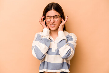 Young hispanic woman isolated on beige background covering ears with hands.