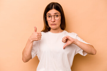 Young hispanic woman isolated on beige background showing thumbs up and thumbs down, difficult...