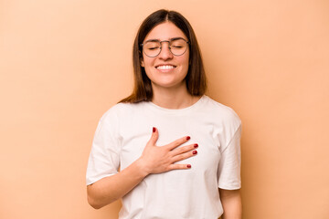 Young hispanic woman isolated on beige background laughs out loudly keeping hand on chest.