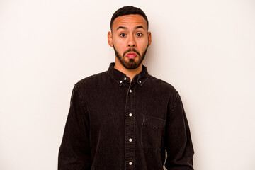 Young hispanic man isolated on white background shrugs shoulders and open eyes confused.