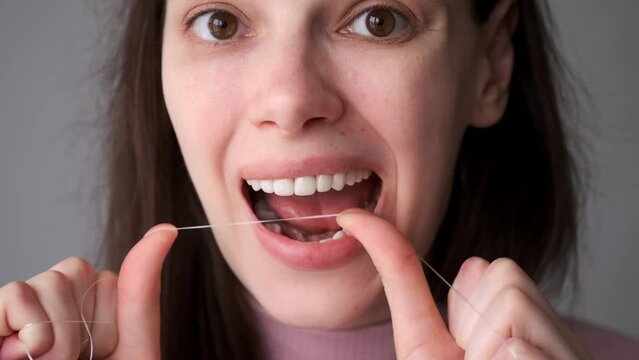 Portrait of young woman is cleaning her white teeth with dental floss smiling in bathroom. Everyday routine, hygiene of oral cavity at home. She is taking care about her teeth.