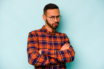 Young hispanic man isolated on blue background suspicious, uncertain, examining you.