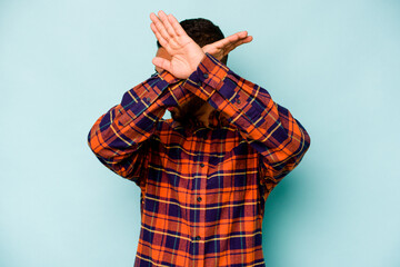 Young hispanic man isolated on blue background keeping two arms crossed, denial concept.