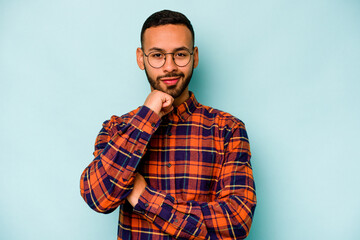 Young hispanic man isolated on blue background smiling happy and confident, touching chin with hand.