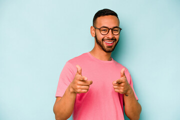 Young hispanic man isolated on blue background pointing to front with fingers.