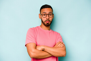 Fototapeta premium Young hispanic man isolated on blue background shrugs shoulders and open eyes confused.