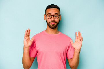 Naklejka premium Young hispanic man isolated on blue background holding something little with forefingers, smiling and confident.