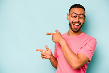 Young hispanic man isolated on blue background excited pointing with forefingers away.