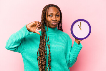 Young African American woman holding a clock isolated on pink background showing a dislike gesture,...
