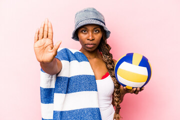 Young African American woman playing volleyball on a beach isolated on pink background standing...