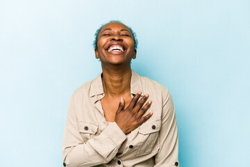 Young african american woman isolated on blue background laughs out loudly keeping hand on chest.