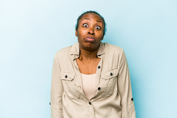 Fototapeta premium Young african american woman isolated on blue background shrugs shoulders and open eyes confused.