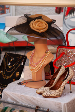 Elegant wide brim vintage ladies hat on mannequin head with pearls and high heeled shoes on side at weekend flea market. Close up image.