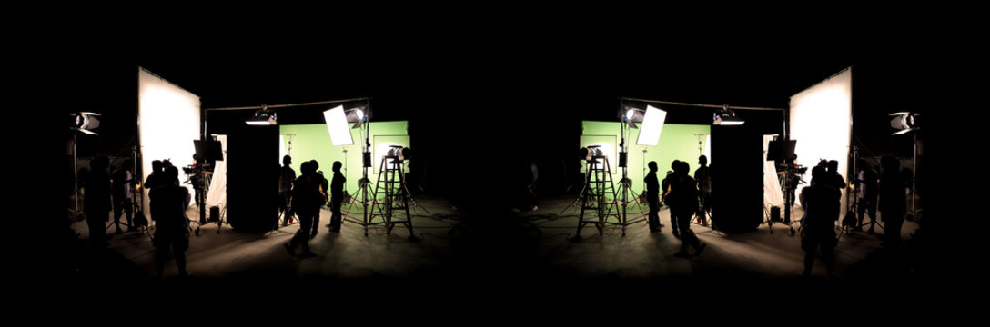 Silhouette images of video production behind the scenes or b-roll or making of TV commercial movie that film crew team lightman and cameraman working together with director in big studio with professi