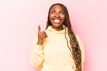Young african american woman isolated on pink background indicates with both fore fingers up...