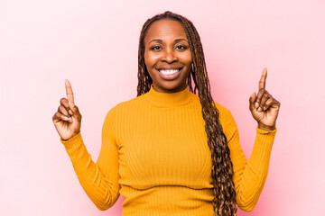 Young african american woman isolated on pink background indicates with both fore fingers up...