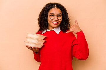 Young African American woman holding tupperware isolated on beige background showing a mobile phone call gesture with fingers.