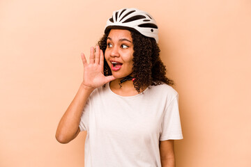 Young hispanic woman wearing a helmet bike isolated on blue background shouting and holding palm near opened mouth.