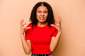 Young African American woman isolated on beige background upset screaming with tense hands.