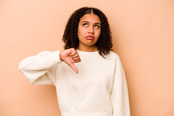 Young African American woman isolated on beige background showing a dislike gesture, thumbs down....
