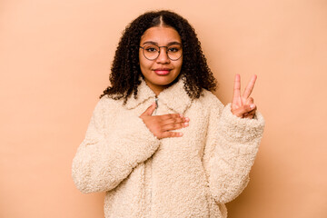 Young African American woman isolated on beige background taking an oath, putting hand on chest.