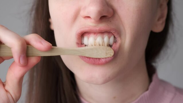 Smiling brunette woman with organic bamboo toothbrush and toothpasteis brushing her white teeth, mouth closeup. Biodegradable ecological personal care products. Plastic free lifestyle concept.