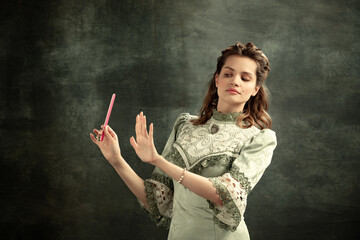 Portrait of young beautiful girl in gray dress of medieval style isolated on dark background. Comparison of eras concept, flemish style. Art, beauty