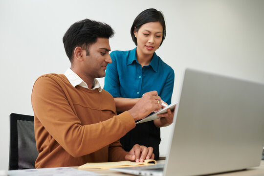 Smiling Indian entrepreneur signing important documant in hands of his assistant