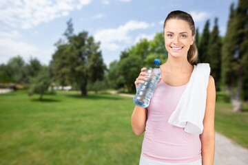 Happy determined athlete, beautiful woman stands on a city and drinks water, resting after early morning jog at sunrise