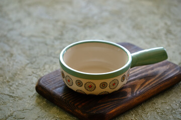 Ceramic bowl with a handle on a wooden board on a concrete table