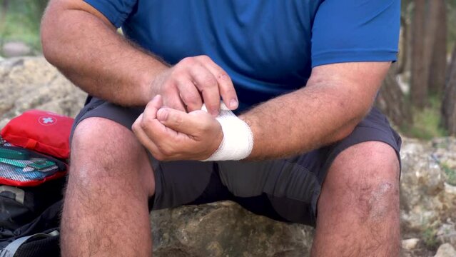 Close up of male hands putting a gauze bandage on an injured wrist.