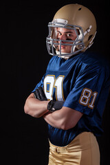 Young football player standing with arms folded looking tough on dark background © Daniel Thornberg
