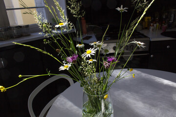 Daisy flower summer bouquet with wild grass into vase on white home kitchen table  
