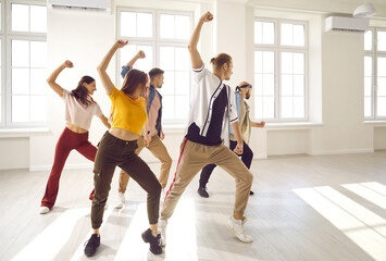 Happy active young people in casual street wear dancing together at class or lesson in studio. Toned millennial teen dancers train show performance for concert. Hobby and activity concept.