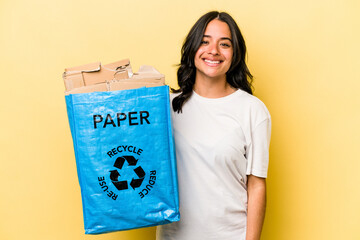 Young hispanic woman recycling paper isolated on yellow background happy, smiling and cheerful.