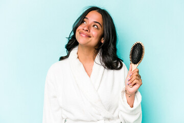 Young hispanic woman holding hairbrush isolated on blue background dreaming of achieving goals and purposes