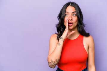 Young hispanic woman isolated on purple background is saying a secret hot braking news and looking...